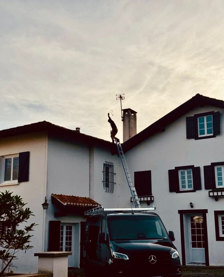 Artisan couvreur Maison Lardeux au travail sur la toiture d'une maison basque, échelle et camion de l'entreprise devant la façade