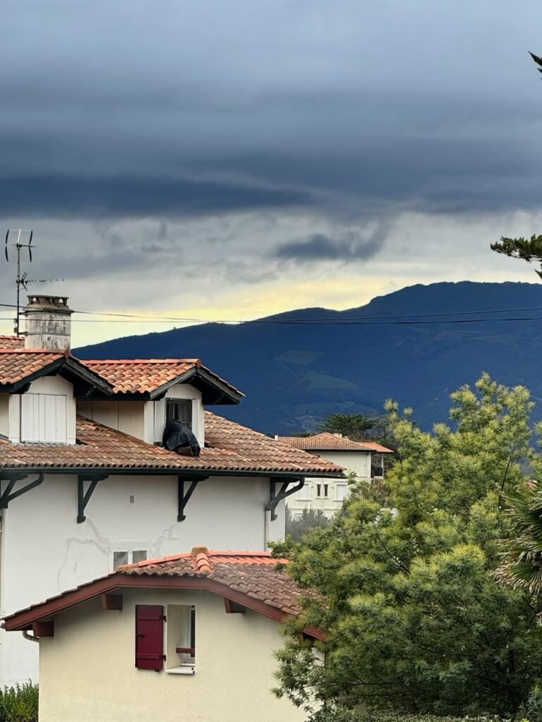 Jordan Lardeux en intervention sur la toiture en tuiles d une batisse basque a Saint-Jean-de-Luz sous un ciel d orage, face a la Rhune